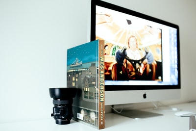 打开iMac，在书旁用黑色相机镜头进行选择性对焦摄影